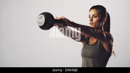 Young fitness female exercise with kettle bell. Mixed race woman doing crossfit workout on grey background. Kettlebell swing. Stock Photo