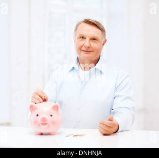 old man putting coin into big piggy bank Stock Photo - Alamy