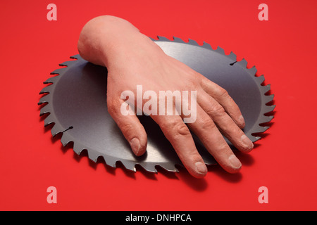 A fake human hand on a metal circular saw blade with a red background. Stock Photo