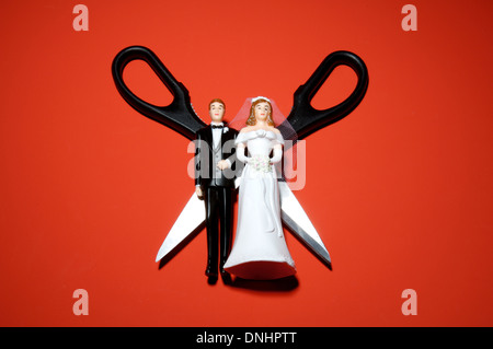 Plastic miniature wedding figures with scissors on a red background. Stock Photo