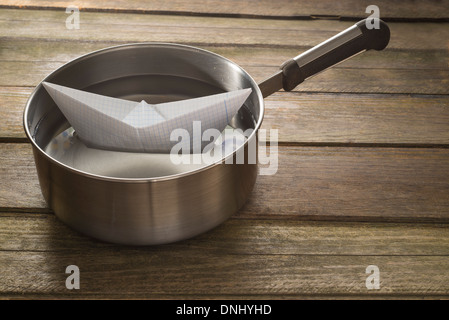 Paper boat sailing in a saucepan. Wooden background Stock Photo