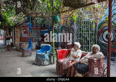 OLD WOMEN SITTING IN FRONT OF THE LA SANTERIA PAINTINGS (CUBAN SYNCRETISM, AFRO-CARABEAN CULTURE), PICTORIAL WORKS BY SALVADOR GONZALEZ ESCALONA PAINTED ON THE CITY'S WALLS, CALLEJON DE HAMEL, HAVANA, CUBA, THE CARIBBEAN Stock Photo