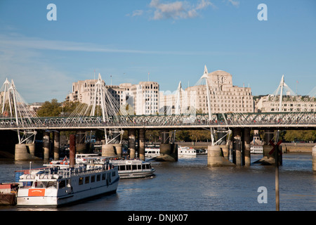View of Hungerford Bridge with tourist boats, a Golden Jubilee Bridge along the south bank, River Thames, London, England, UK.