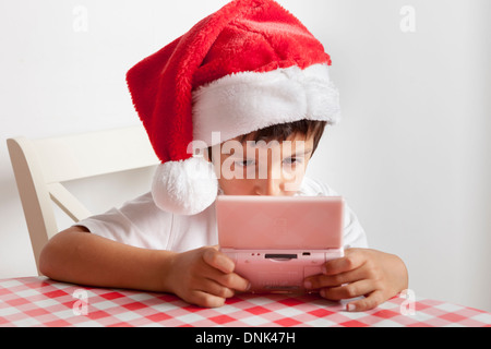 Boy in Santa's hat plays on Nintendo DS Stock Photo