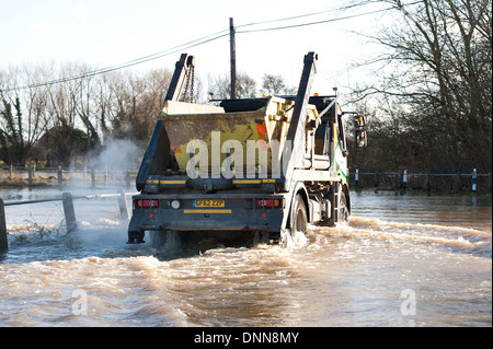 Skip lorry vehicle truck travels down submerged Hampstead lane road deep water Stock Photo