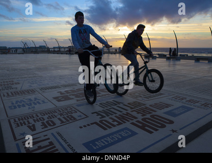 Teenage Boys performing bicycle tricks on the Blackpool Comedy Carpet or Pavement at sunset. Lancashire, UK Stock Photo