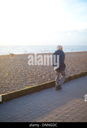 A male pensioner takes his dog for a walk on Brighton promenade at sunset on Christmas Day Stock Photo