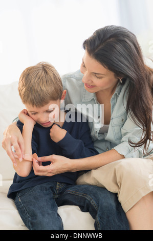 Mother helping son (6-7) put on bandaid Stock Photo