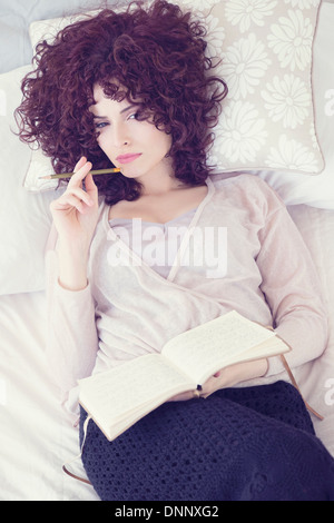 Portrait of beautiful brunette woman lying on bed with diary Stock Photo