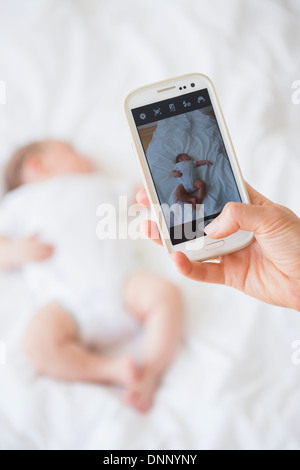 Mother photographing baby girl (2-5 months) sleeping in bed Stock Photo