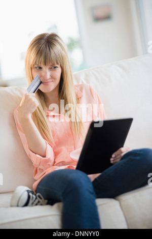 Woman sitting on sofa holding credit card and tablet pc Stock Photo