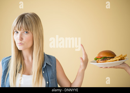 Portrait of woman rejecting hamburger that is being offered to her Stock Photo