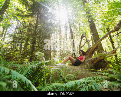 USA, Oregon, Portland, Young woman reading book on log in forest Stock Photo