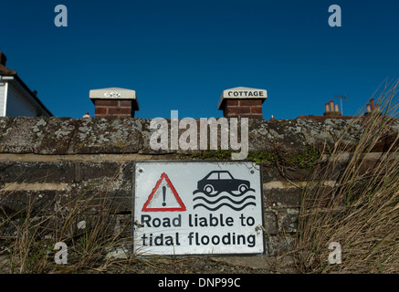 A sign warning of the danger of flooding on a wall next to a coastal road at Bosham, West Sussex, England, United Kingdom. Stock Photo