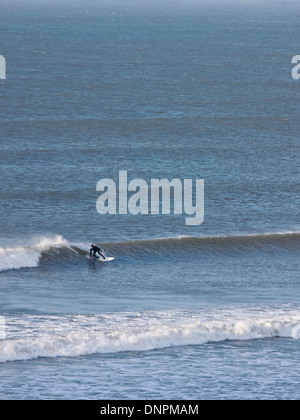 A lone surfer riding a wave off the North Devon coast at Putsborough. This stretch of coast is popular with surfers in the UK Stock Photo