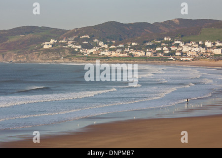 A lone surfer makes their way into the sea on a winter's afternoon at Woolacombe Bay in North Devon UK Stock Photo