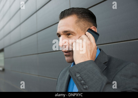 Close-up portrait of businessman standing in front of wall of building using cell phone, Mannheim, Germany Stock Photo