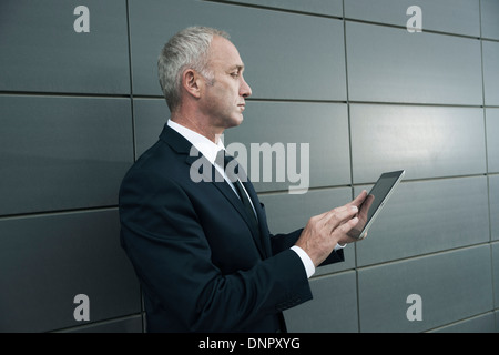 Mature businessman standing in front of wall, looking at tablet computer Stock Photo