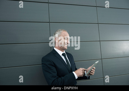 Mature businessman standing in front of wall, looking at tablet computer Stock Photo