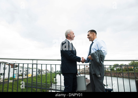 Mature businessmen standing by railing, shaking hands outdoors, Mannheim, Germany Stock Photo