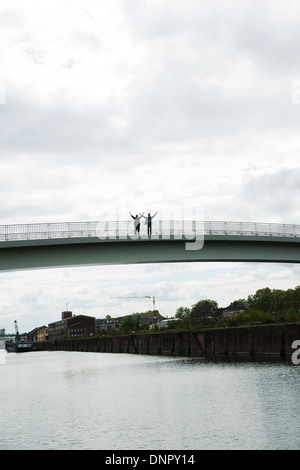 Silhouette of mature businessmen standing on bridge with arms in air, Mannheim, Germany Stock Photo