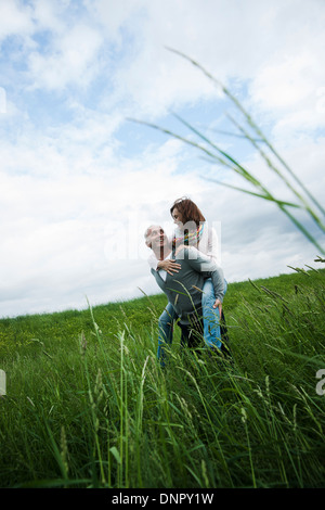 Mature couple in field of grass, man giving piggyback ride to woman, Germany Stock Photo