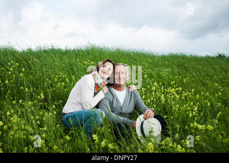 Portrait of mature couple sitting in field of grass, embracing, Germany Stock Photo