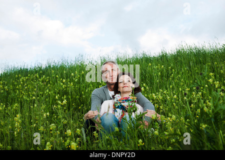 Portrait of mature couple sitting in field of grass, embracing, Germany Stock Photo