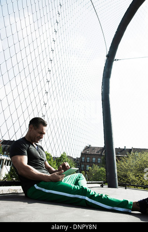 Mature man sitting on outdoor basketball court, looking at tablet computer, Germany Stock Photo