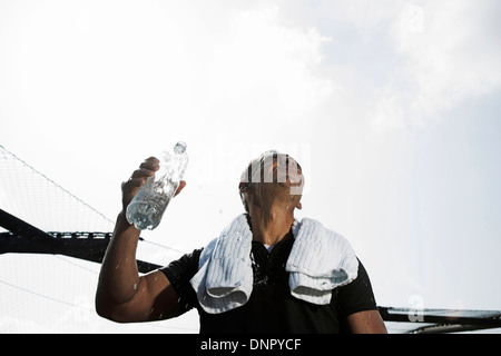 Mature man with towel around neck, holding bottle of water and looking up at sky, Germany Stock Photo
