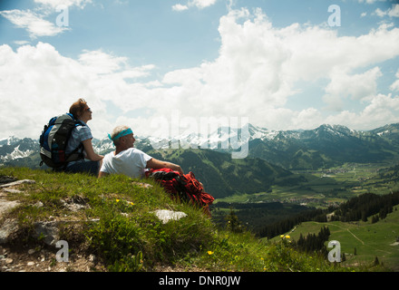 Backview of mature couple sitting on grass, hiking in mountains, Tannheim Valley, Austria Stock Photo
