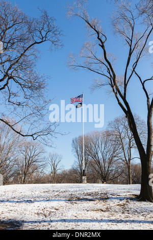 American Stars & Stripes national flag flying from flagpole in Central Park, New York against a blue sky with snow on ground Stock Photo