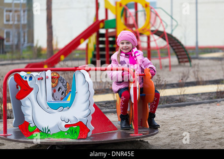 Little girl on the carousel in the autumn clothes Stock Photo