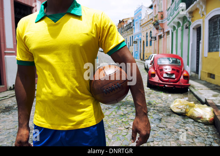 Brazilian soccer player standing on colonial Bahia street Pelourinho Salvador with vintage football Stock Photo