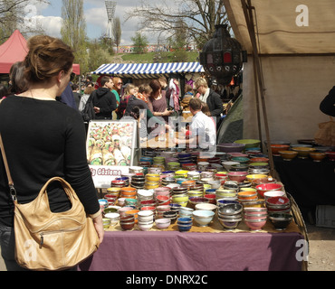 Sunny view young woman standing market stall table with colourful pots, towards people walkiing, Mauerpark Flea Market, Berlin Stock Photo