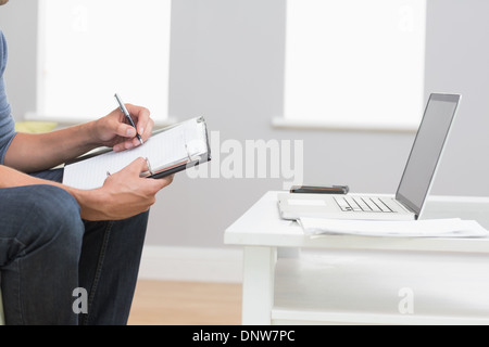 Mid section of a man with laptop writing in diary at home Stock Photo