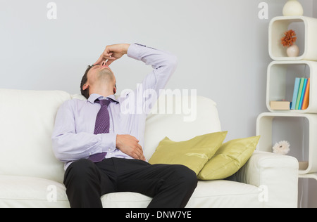 Tired businessman sitting on sofa in living room Stock Photo