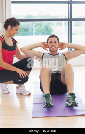 Female trainer watching man do abdominal crunches  on exercise mat Stock Photo