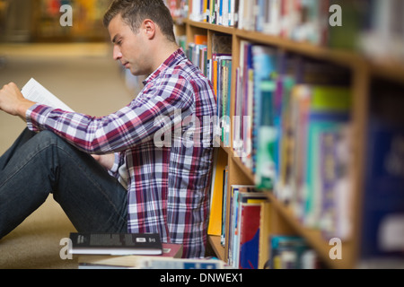Focused young student sitting on library floor reading Stock Photo