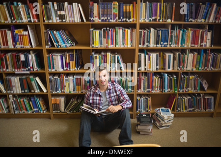 Smiling young student sitting on library floor reading Stock Photo