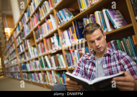 Focused young student sitting on library floor reading book Stock Photo