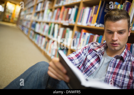 Serious young student sitting on library floor reading book Stock Photo