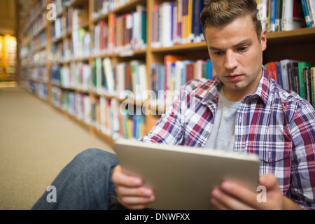 Serious young student sitting on library floor using tablet Stock Photo
