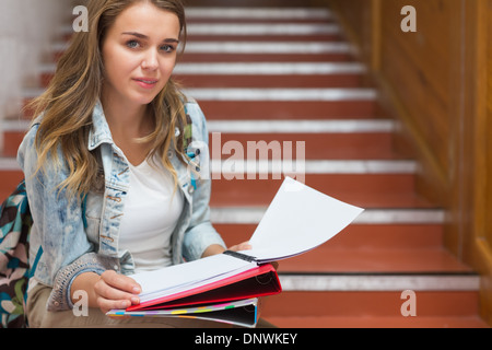 Smiling young student sitting on stairs looking at camera Stock Photo