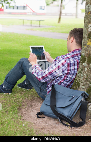 Student using his tablet pc outside leaning on tree Stock Photo