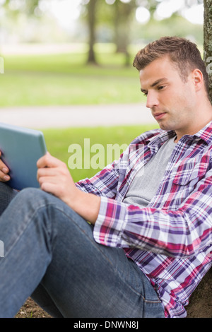Serious student using his tablet pc outside leaning on tree Stock Photo