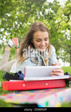 Pretty student lying on the grass studying with her tablet pc Stock Photo