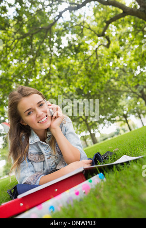 Young smiling student lying on the grass on the phone Stock Photo