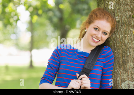 Cheerful redhead student leaning against a tree Stock Photo