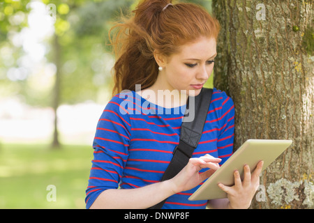 Redhead student leaning against a tree using her tablet Stock Photo
